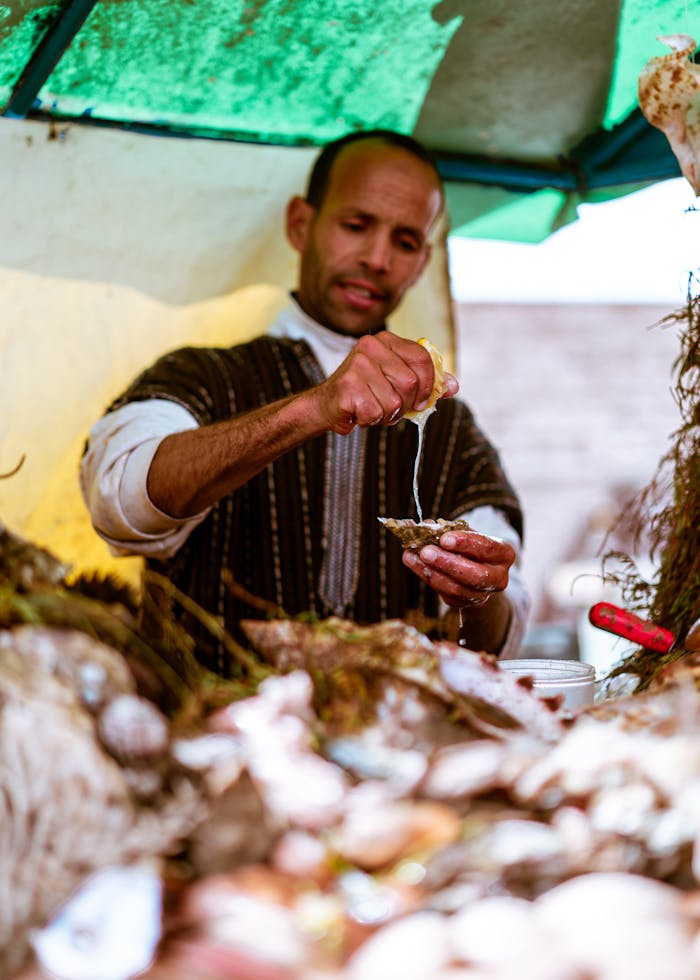 Vendor squeezing lemon over seafood in Essaouira market stall, Morocco.